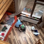 Співробітниця клінінгової компанії Юнона за допомогою професійного пилососа вичищає пил з радіатора опалення в дерев'яному будинку.