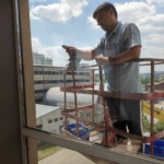 Співробітник компанії Юнона виконує професійне миття панорамних вікон на висоті за допомогою спеціальної підйомної вишки.